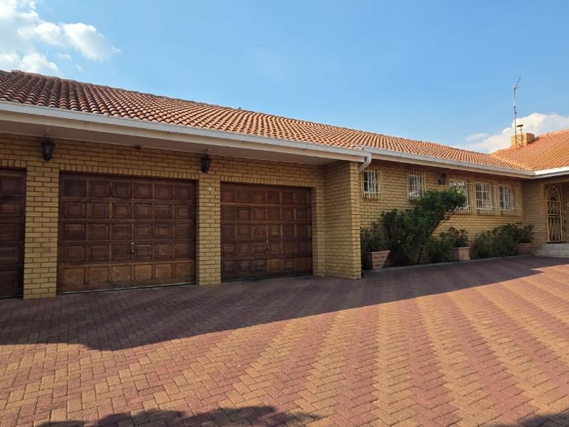 Front elevation of a brick house featuring a triple garage, tiled roof, and a spacious paved driveway.