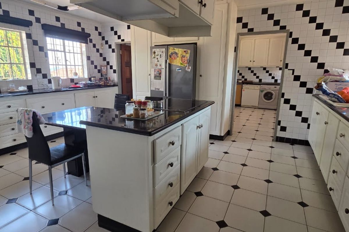 Spacious kitchen featuring a central island, granite countertops, ample built-in cabinetry, and a distinct black and white tiled design, with an adjoining laundry area.