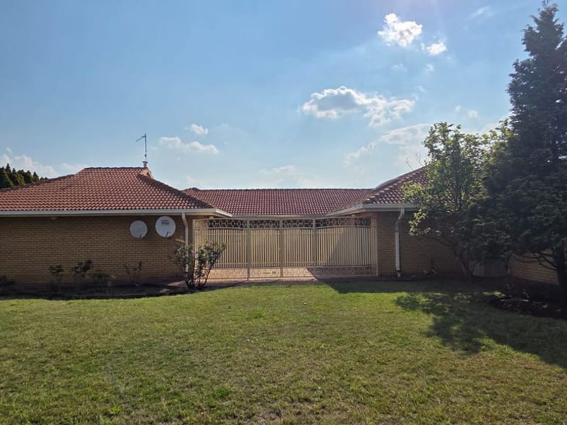 Rear view of a single-story brick house featuring a tiled roof, security gate, and a spacious lawn area.