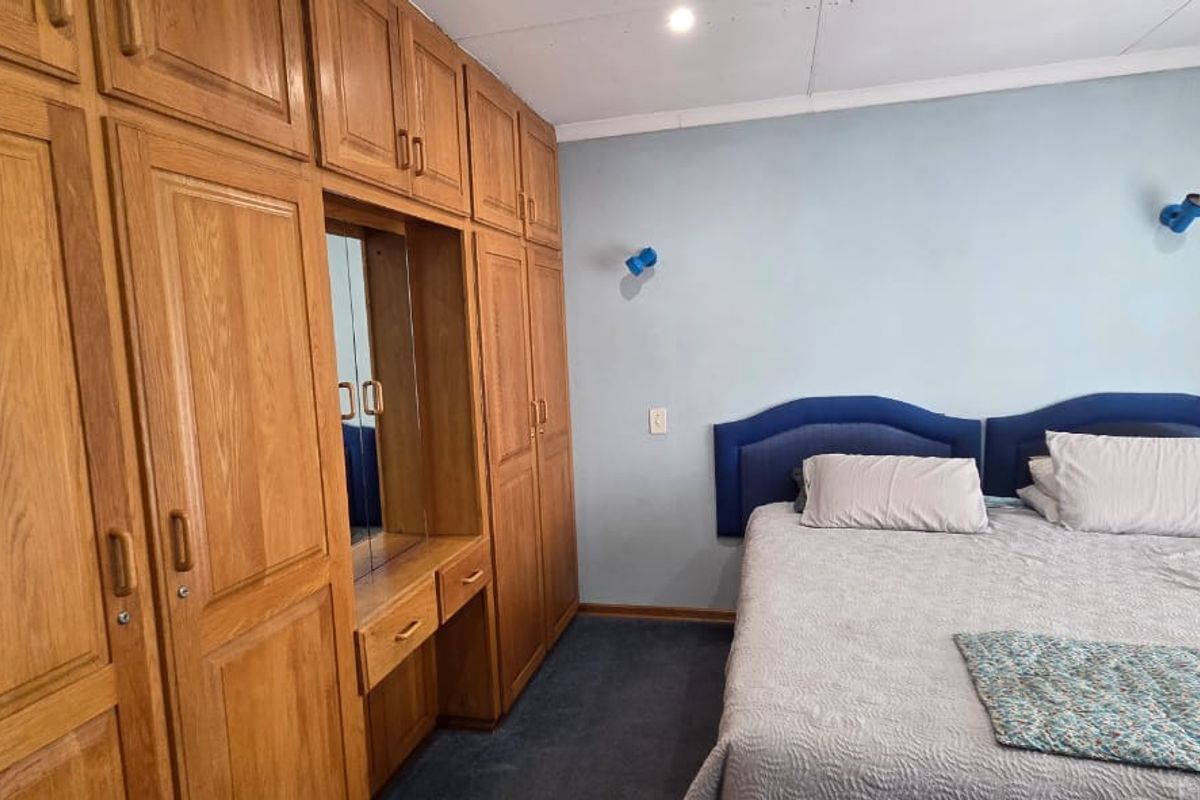 A bedroom featuring extensive built-in wooden cabinetry with an integrated vanity, blue wall accents, and carpeted flooring.