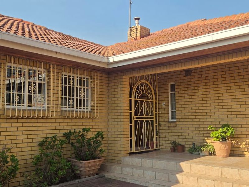 Front entrance of a face brick house featuring a tiled porch, security gate, and protective window bars.