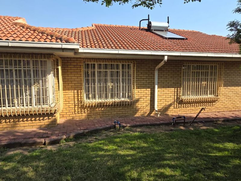 Rear view of a brick house featuring a tiled roof with a solar water heater, security bars on windows, and a paved walkway.