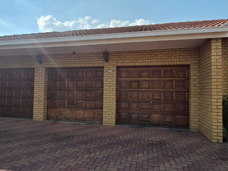 A triple garage featuring wooden panelled doors, a brick exterior, and a paved driveway, providing secure parking space.
