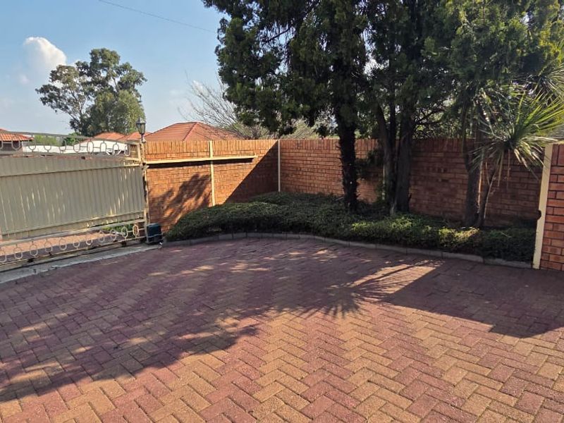 A paved front driveway area featuring a secure sliding gate and a brick boundary wall with established trees.