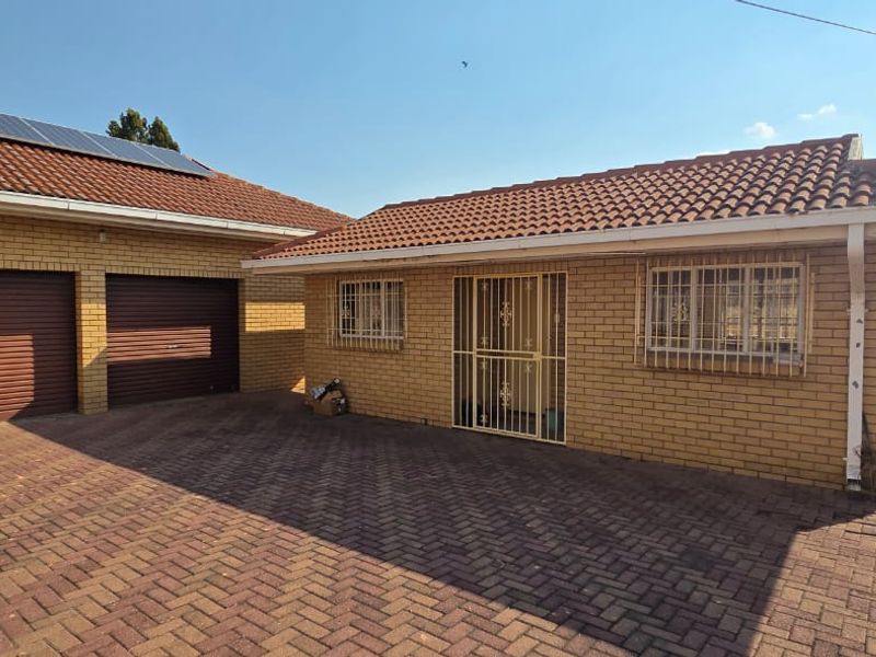 Front exterior view of a brick house featuring a double garage, paved driveway, and solar panels installed on the tiled roof.
