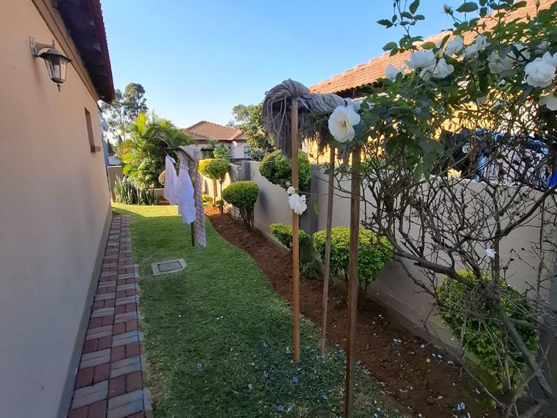 A side garden pathway featuring a paved walkway, boundary wall, and established landscaping along the side of the house.