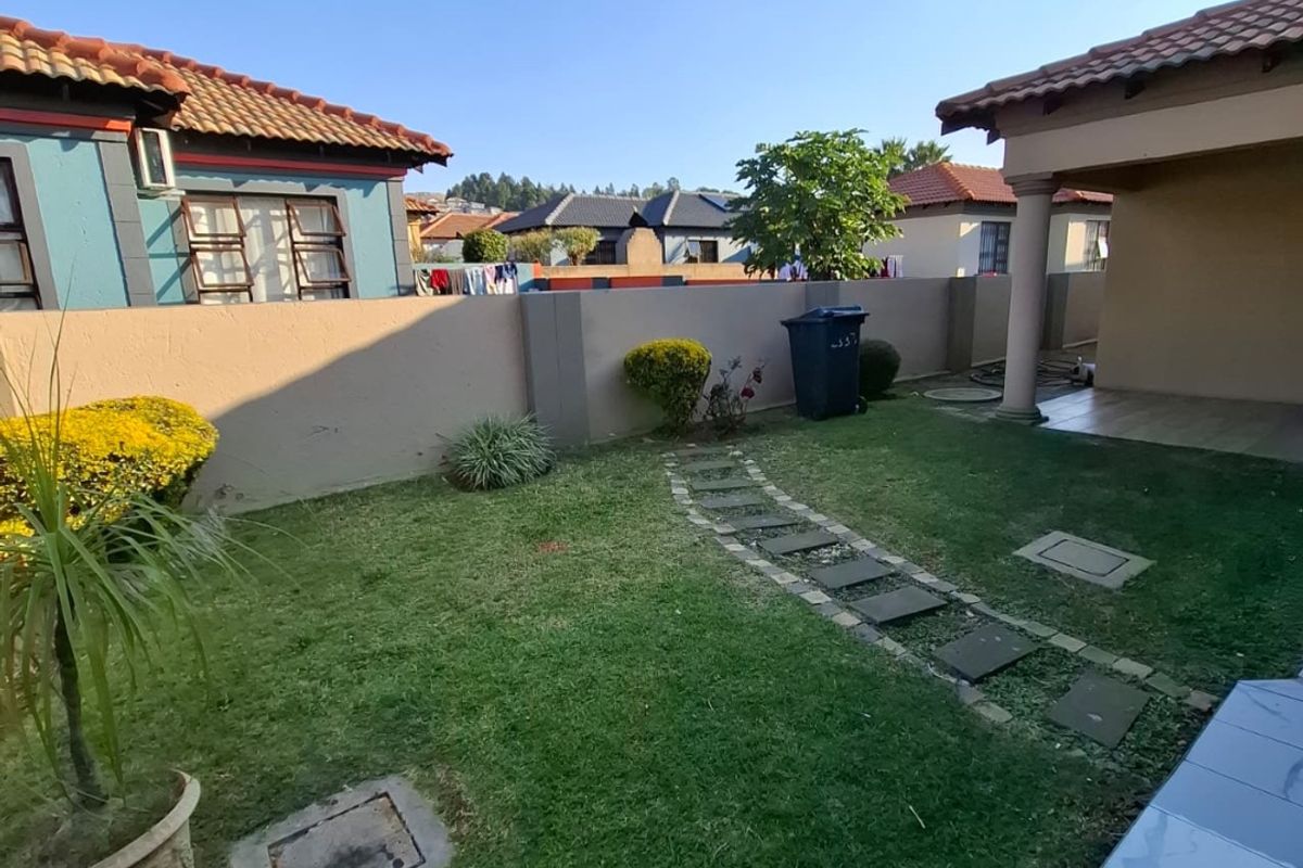 A private rear garden featuring a lawn, paved stepping stone path, boundary wall, and a covered patio area with tiled flooring.