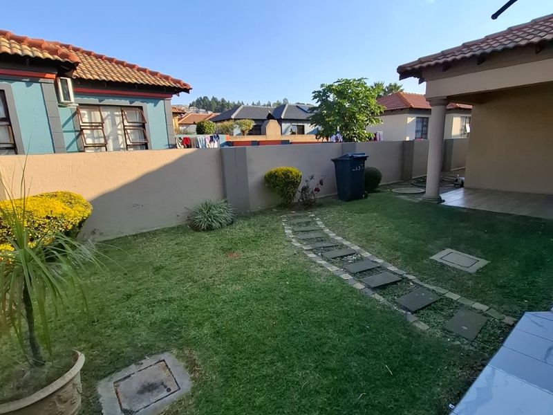 A private rear garden featuring a lawn, paved stepping stone path, boundary wall, and a covered patio area with tiled flooring.