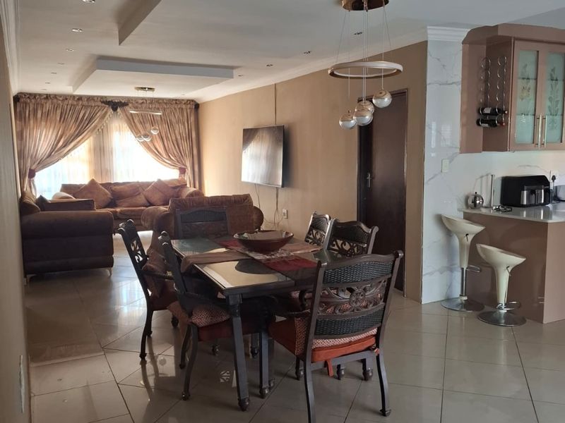 An open-plan living and dining area featuring tiled floors, recessed ceiling lighting, and a functional kitchen with a breakfast bar and built-in cabinetry.