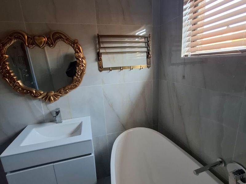 Modern bathroom featuring a sleek freestanding bathtub, wall-mounted vanity with basin, and elegant tiled finishes.