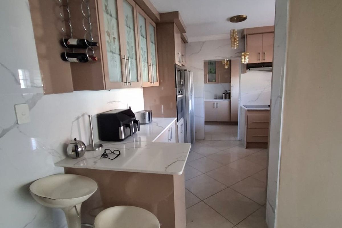 A functional kitchen featuring built-in cabinetry, stone countertops, and marble-look wall finishes, with an adjacent scullery area visible through the doorway.