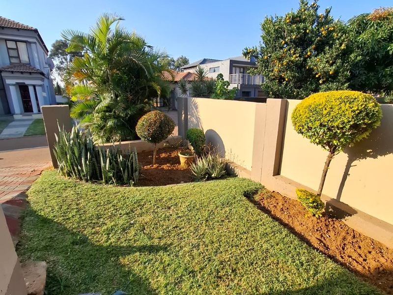 A well-maintained front garden featuring a manicured lawn, established shrubs, and a solid boundary wall.