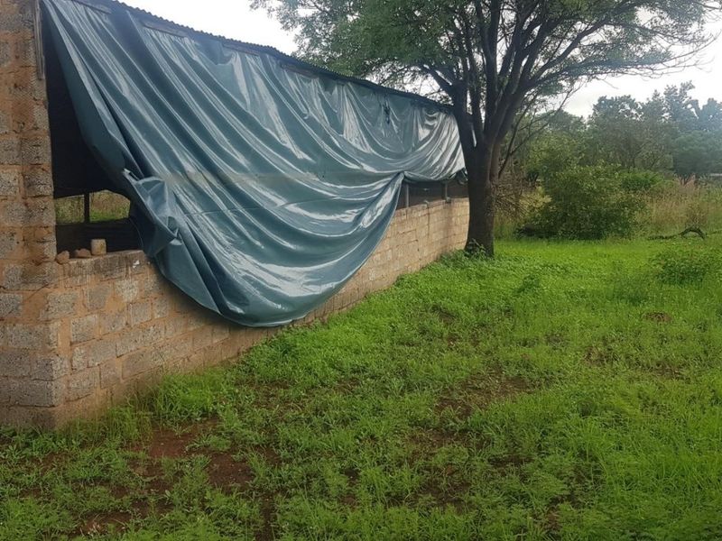 A basic utility structure on the farm property featuring cinder block walls and a corrugated metal roof, currently requiring significant maintenance and repair.