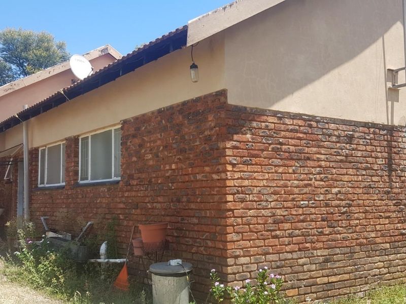 Rear exterior view of a farm dwelling featuring face brick construction, metal window frames, and a tiled roof requiring maintenance on fascia boards.