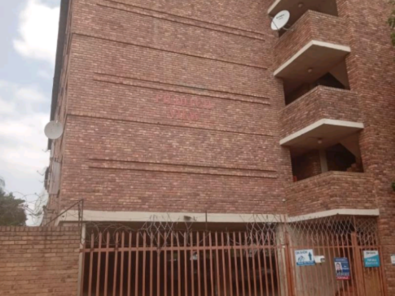 Exterior view of a multi-story apartment building featuring face brick construction, private balconies, and a secure gated parking entrance.