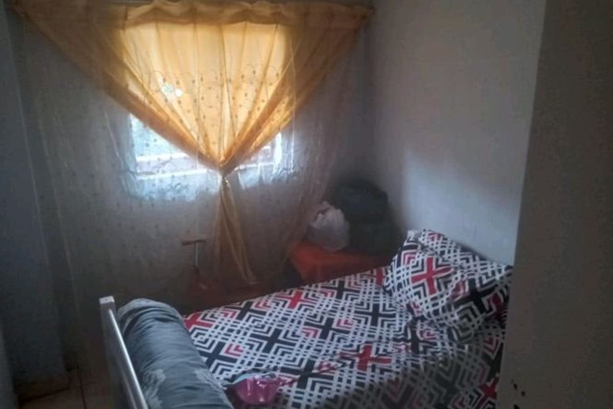 A compact bedroom featuring tiled flooring and a window fitted with security bars, offering a functional space for a single bed.