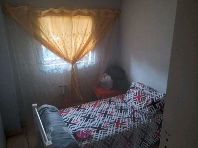 A compact bedroom featuring tiled flooring and a window fitted with security bars, offering a functional space for a single bed.
