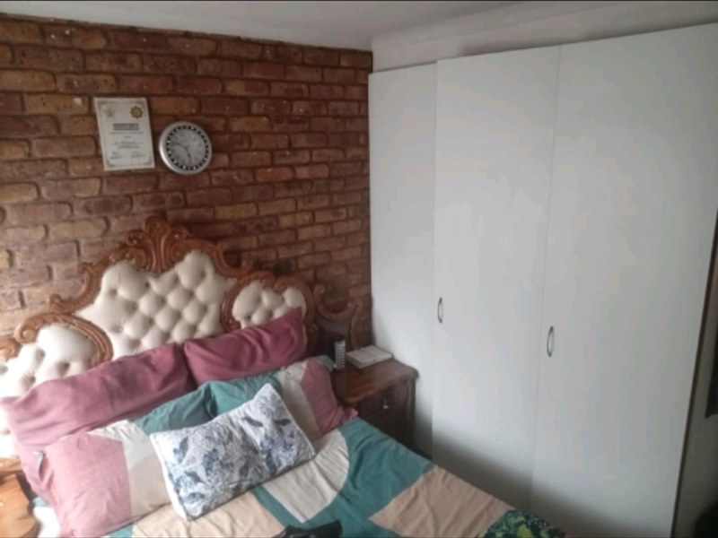 Bedroom featuring an exposed brick feature wall and white built-in wardrobes.