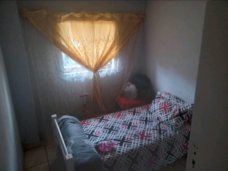 A compact bedroom featuring tiled flooring and a window with decorative curtains.