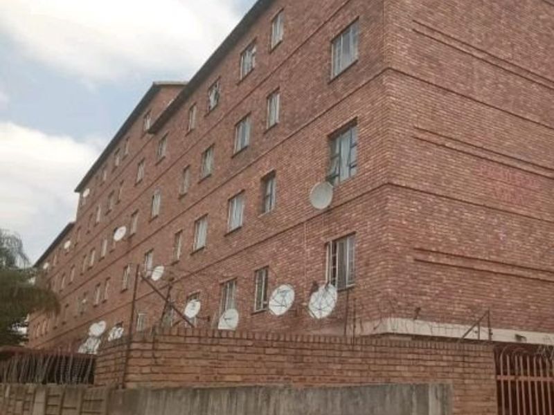 Exterior view of a multi-story face brick apartment building featuring security fencing and multiple satellite dish installations.