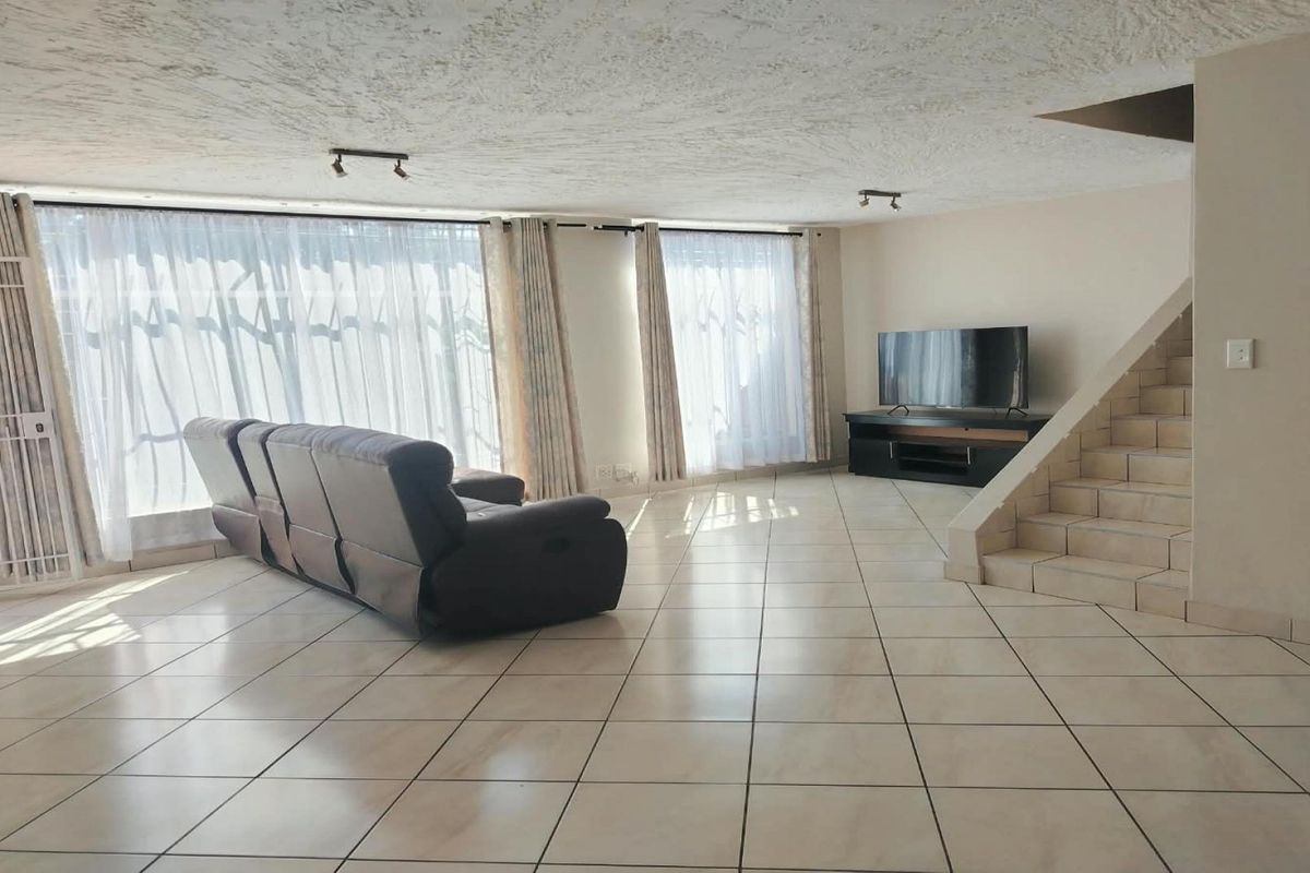 Spacious living area featuring tiled flooring, a built-in staircase, and large windows with natural light, providing a versatile open-plan layout.