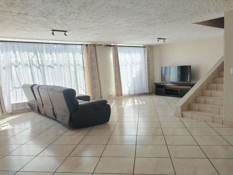 Spacious living area featuring tiled flooring, a built-in staircase, and large windows with natural light, providing a versatile open-plan layout.