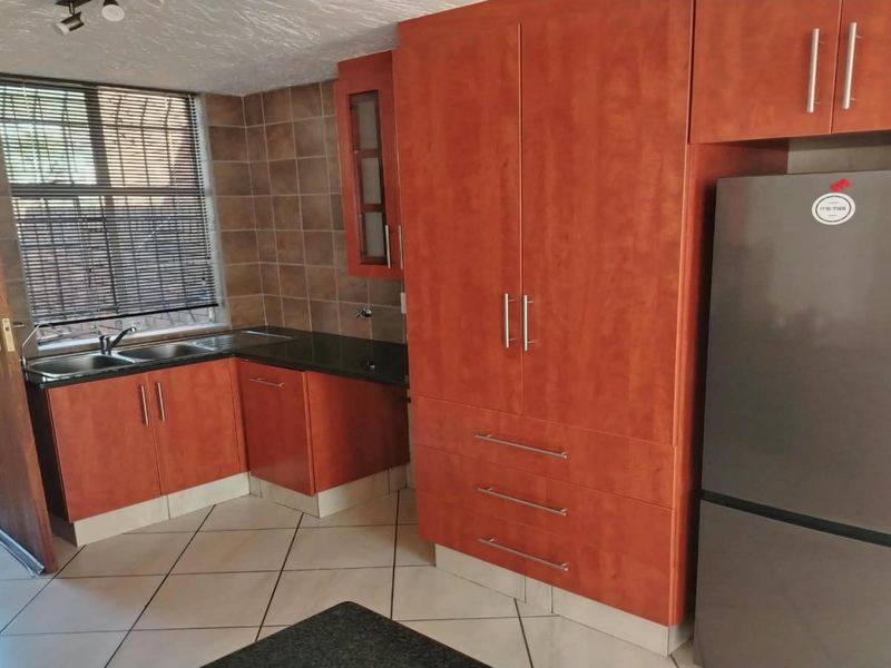 A functional kitchen featuring warm-toned laminate cabinetry, granite countertops, tiled backsplash, and ceramic flooring with direct access to an outdoor area.