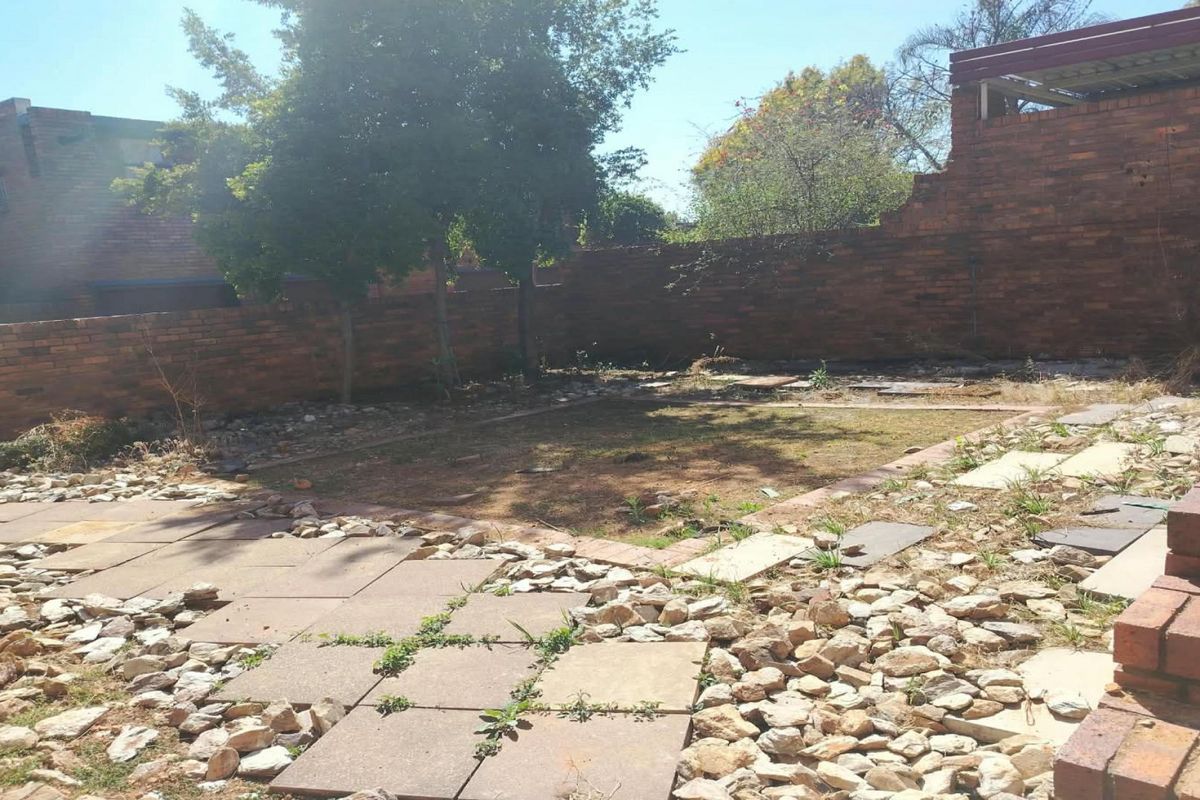 A private rear garden featuring a brick boundary wall, paved patio area, and established trees, offering potential for landscaping and outdoor improvement.