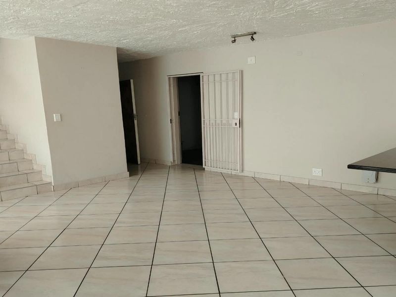 Spacious open-plan living area featuring tiled flooring, a built-in breakfast bar, and a staircase leading to the upper level.