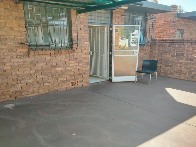 A paved outdoor patio area featuring exposed brick walls, security gates, and protective window bars, offering a functional space for outdoor living.