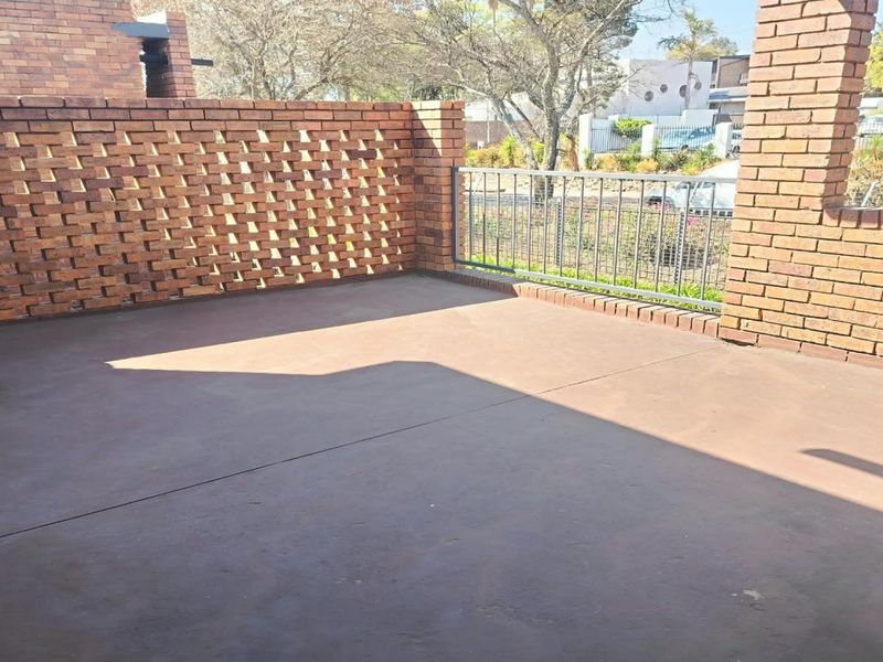 An open-air patio featuring exposed brick walls and metal railings, providing a private outdoor space with concrete flooring.