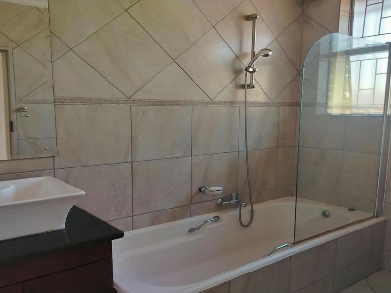 A functional bathroom featuring a vessel sink on a vanity, a bathtub with a glass shower screen, and tiled wall finishes.