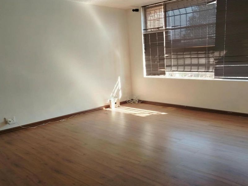 A bright, empty living room featuring laminate flooring, neutral walls, and fitted venetian blinds, offering a clean canvas for interior design.