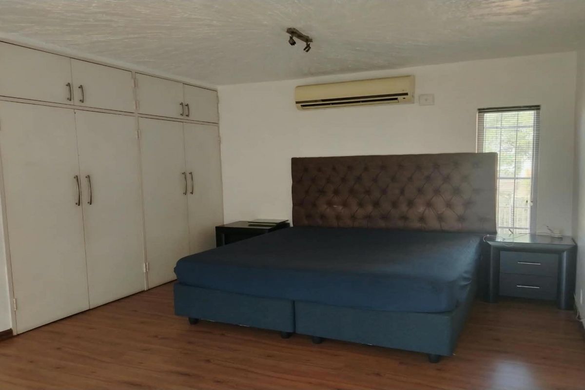 Spacious bedroom featuring laminate flooring, extensive built-in cupboard storage, and a wall-mounted split-system air conditioning unit.