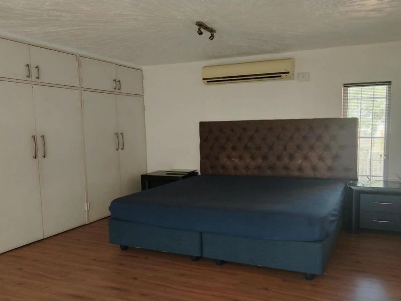 Spacious bedroom featuring laminate flooring, extensive built-in cupboard storage, and a wall-mounted split-system air conditioning unit.