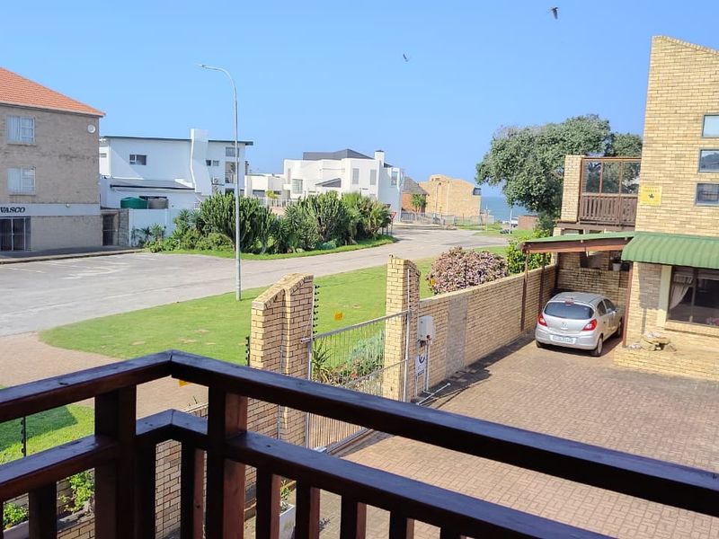 Elevated view from a balcony overlooking a paved driveway, brick boundary wall, and the surrounding residential streetscape.