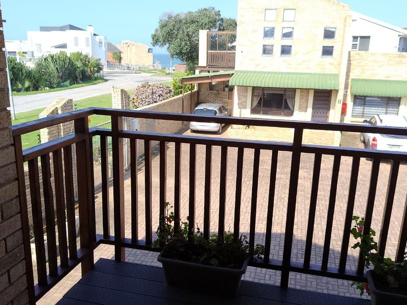 An elevated timber balcony overlooking a paved driveway and neighbouring townhouse complex with partial sea views in the distance.
