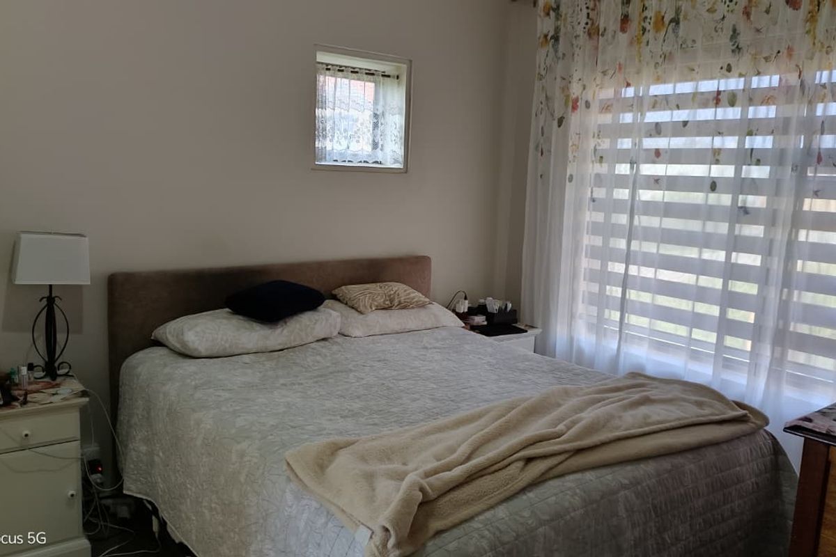 A functional bedroom featuring a large window with blinds and an additional small square window, providing natural light to the space.
