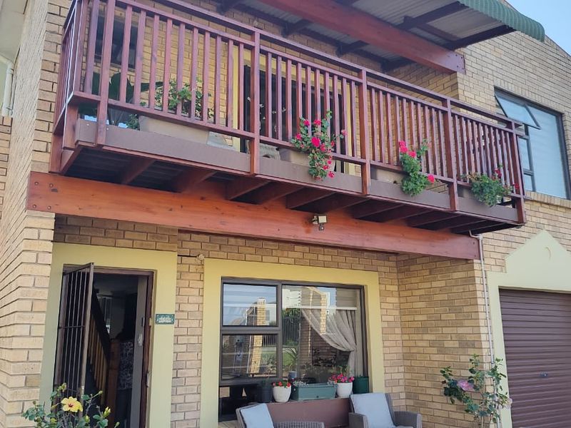 Front elevation of a brick townhouse featuring a prominent timber balcony, secure entrance, and integrated garage.
