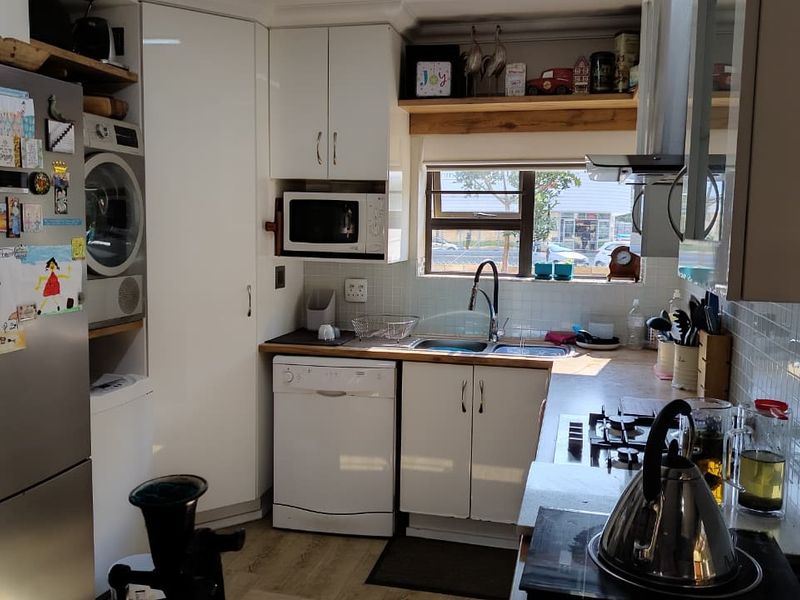 Compact kitchen featuring white cabinetry, laminate countertops, tiled backsplash, and integrated laundry space with a gas hob and built-in oven.