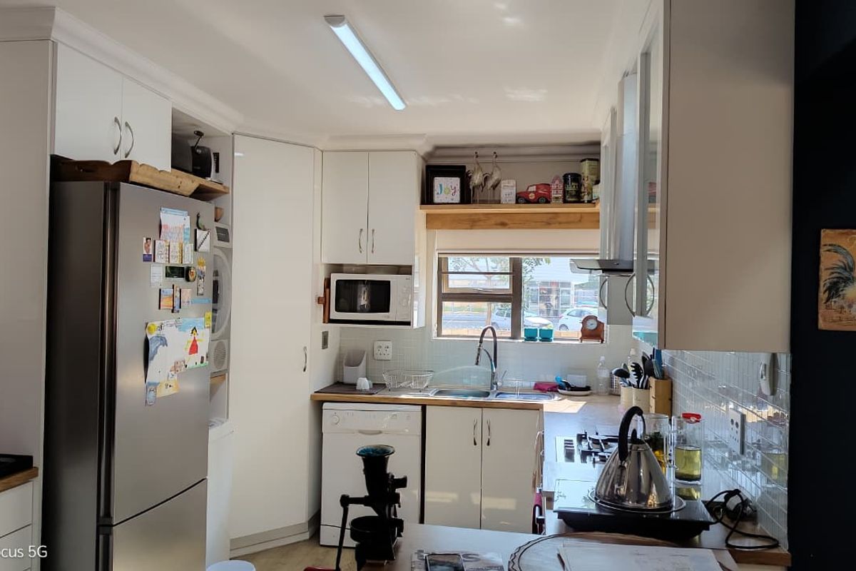 A functional kitchen featuring white cabinetry, tiled splashbacks, a double sink, and integrated appliances, offering a clean and practical workspace.