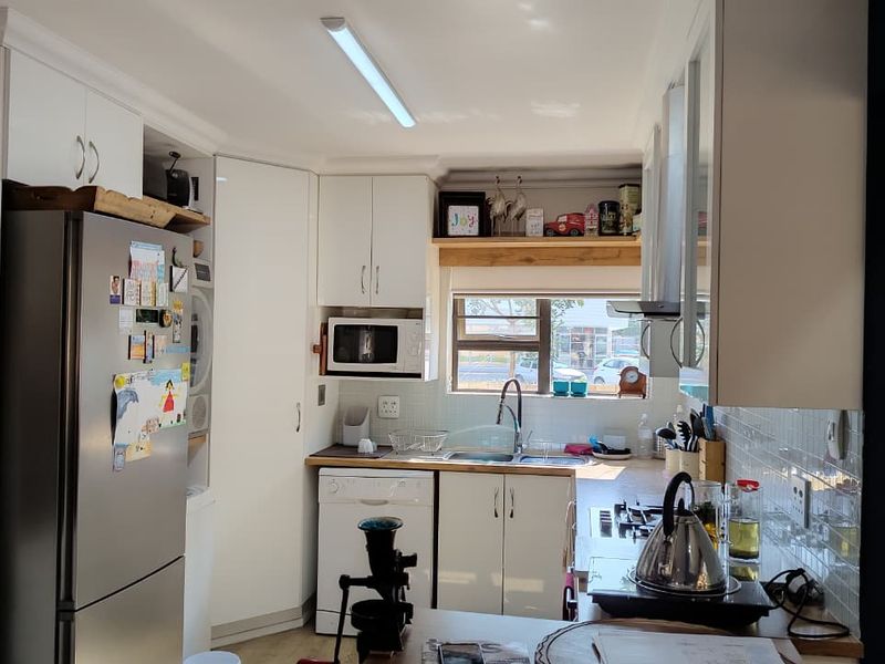 A functional kitchen featuring white cabinetry, tiled splashbacks, a double sink, and integrated appliances, offering a clean and practical workspace.