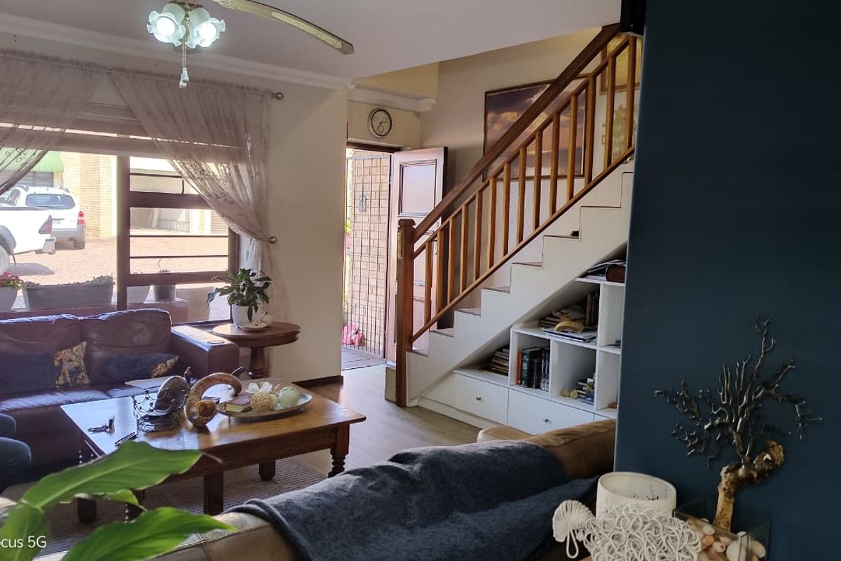 A living room featuring a wooden staircase with integrated under-stair storage, a ceiling fan, and natural light from a large window.