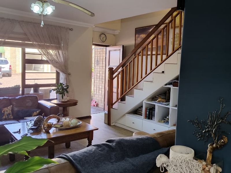 A living room featuring a wooden staircase with integrated under-stair storage, a ceiling fan, and natural light from a large window.