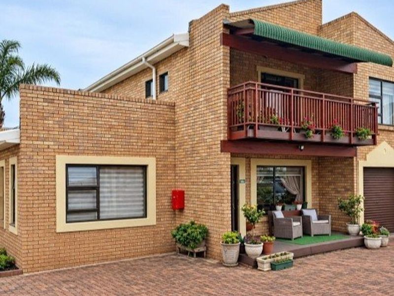 A well-maintained brick townhouse featuring a paved driveway, a private balcony with timber railings, and a green awning over the upper level.