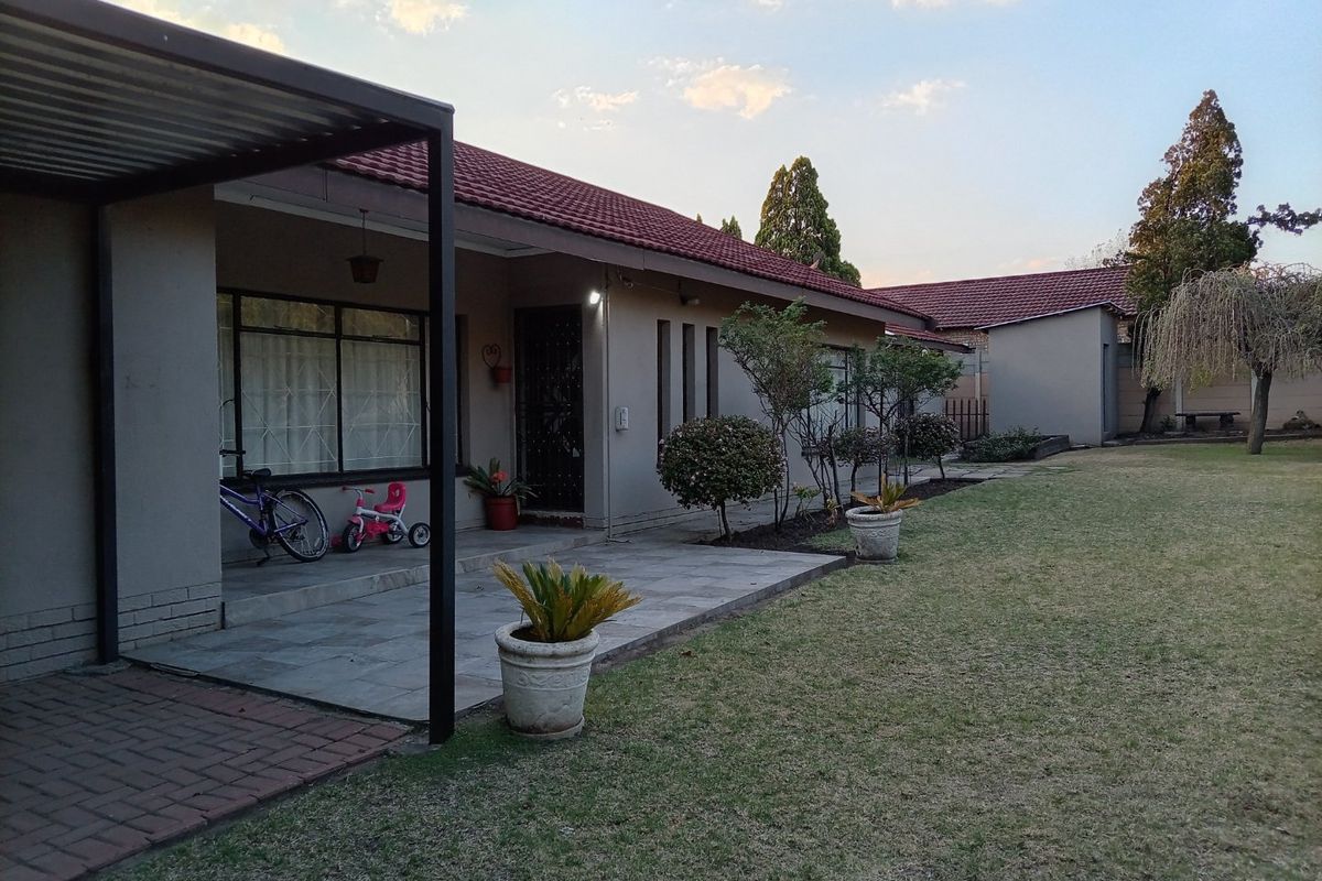 Rear view of the property featuring a covered tiled patio, paved walkway, and a well-maintained garden area.