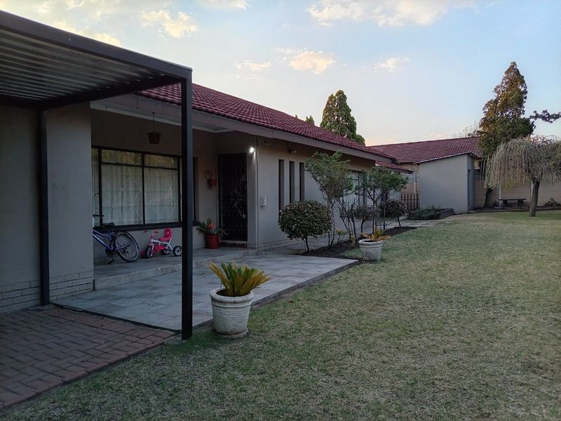 Rear view of the property featuring a covered tiled patio, paved walkway, and a well-maintained garden area.