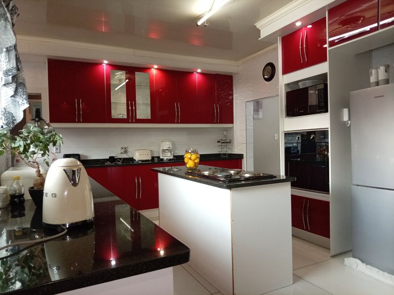 Modern kitchen featuring high-gloss red cabinetry, granite countertops, a central island with a built-in hob, and integrated appliances.