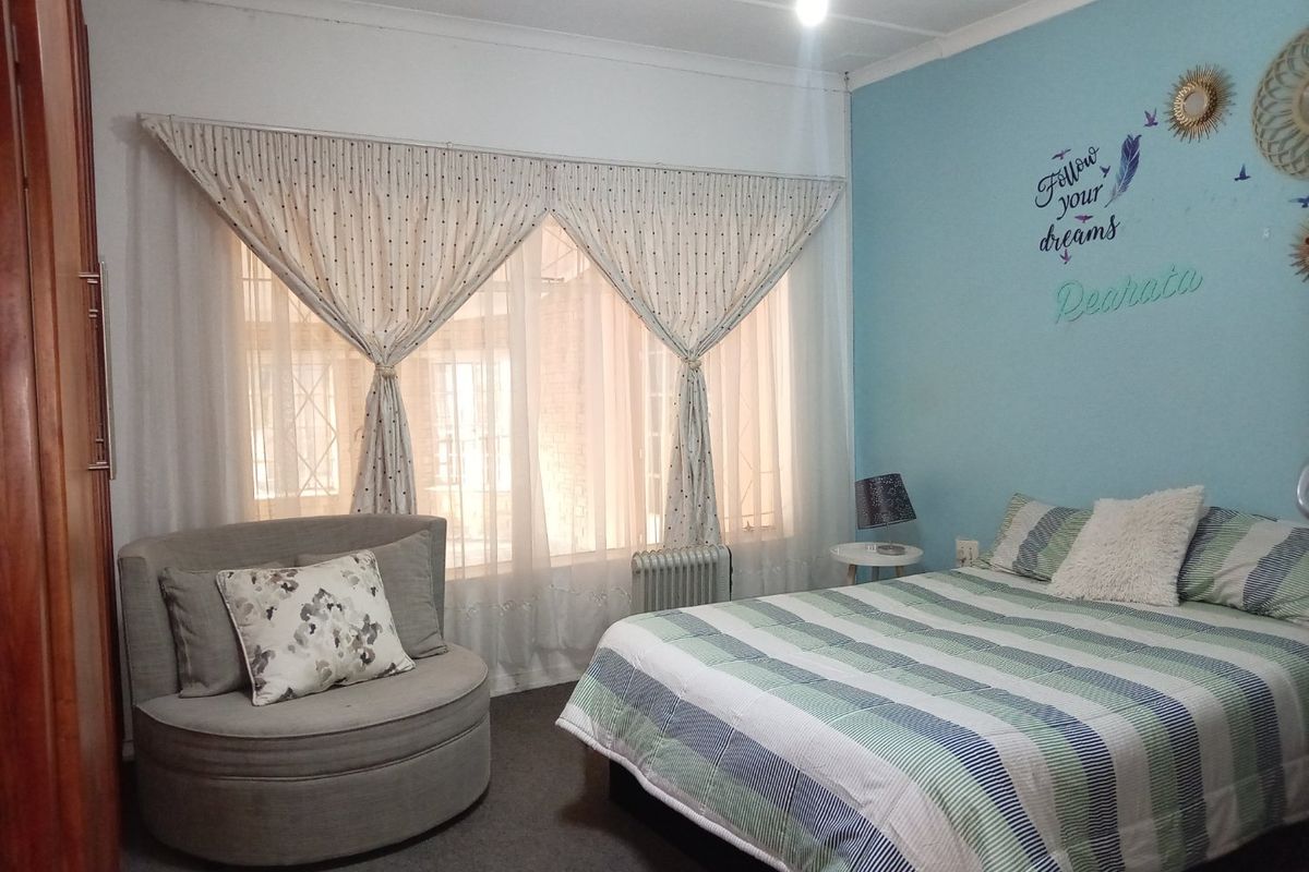 A cozy bedroom featuring a built-in wardrobe, a radiator, and large windows with curtains, providing a comfortable and functional living space.