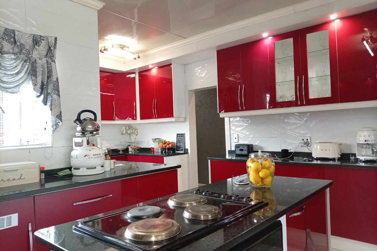 Modern kitchen featuring high-gloss red cabinetry, black granite countertops, a central island with an integrated hob, and tiled backsplash.